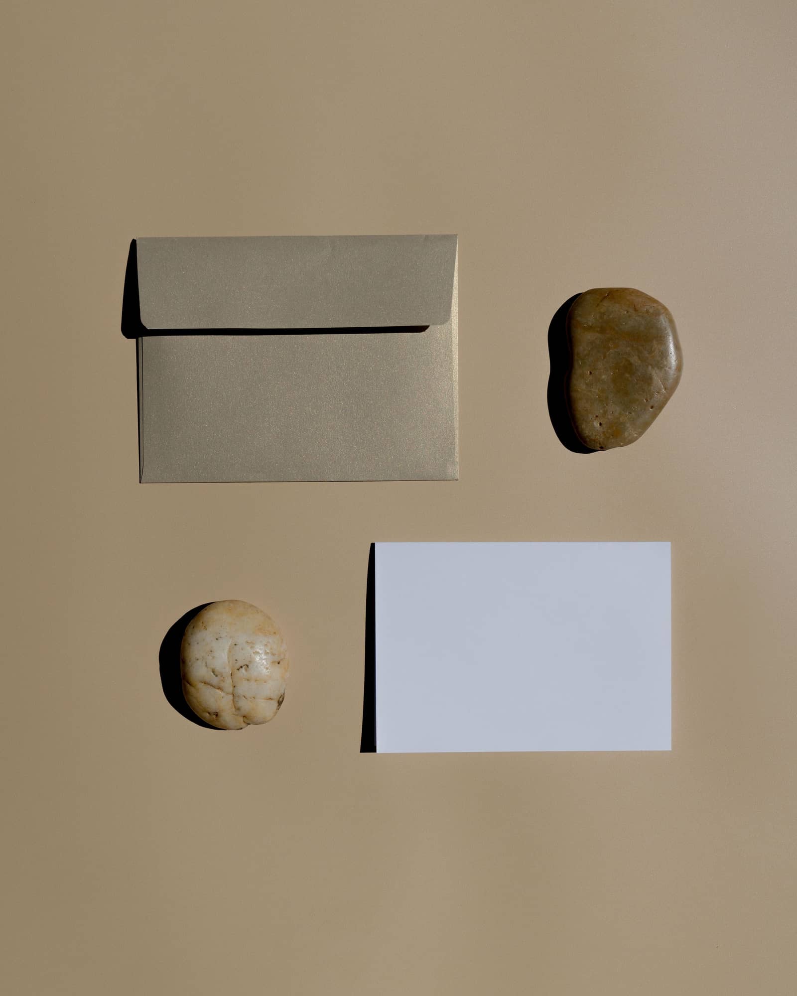 Enveloppe, carte vierge et deux galets posés sur un fond sable